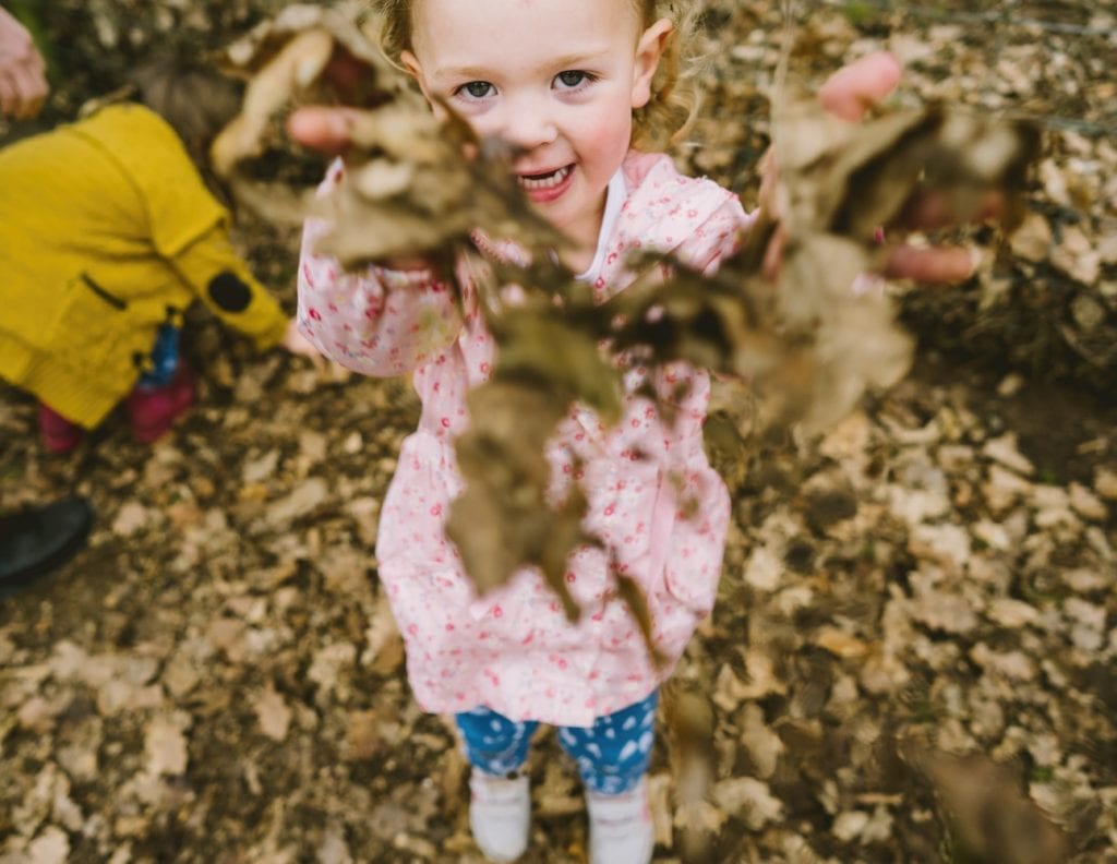Little girl throws autumn leaves at the camera