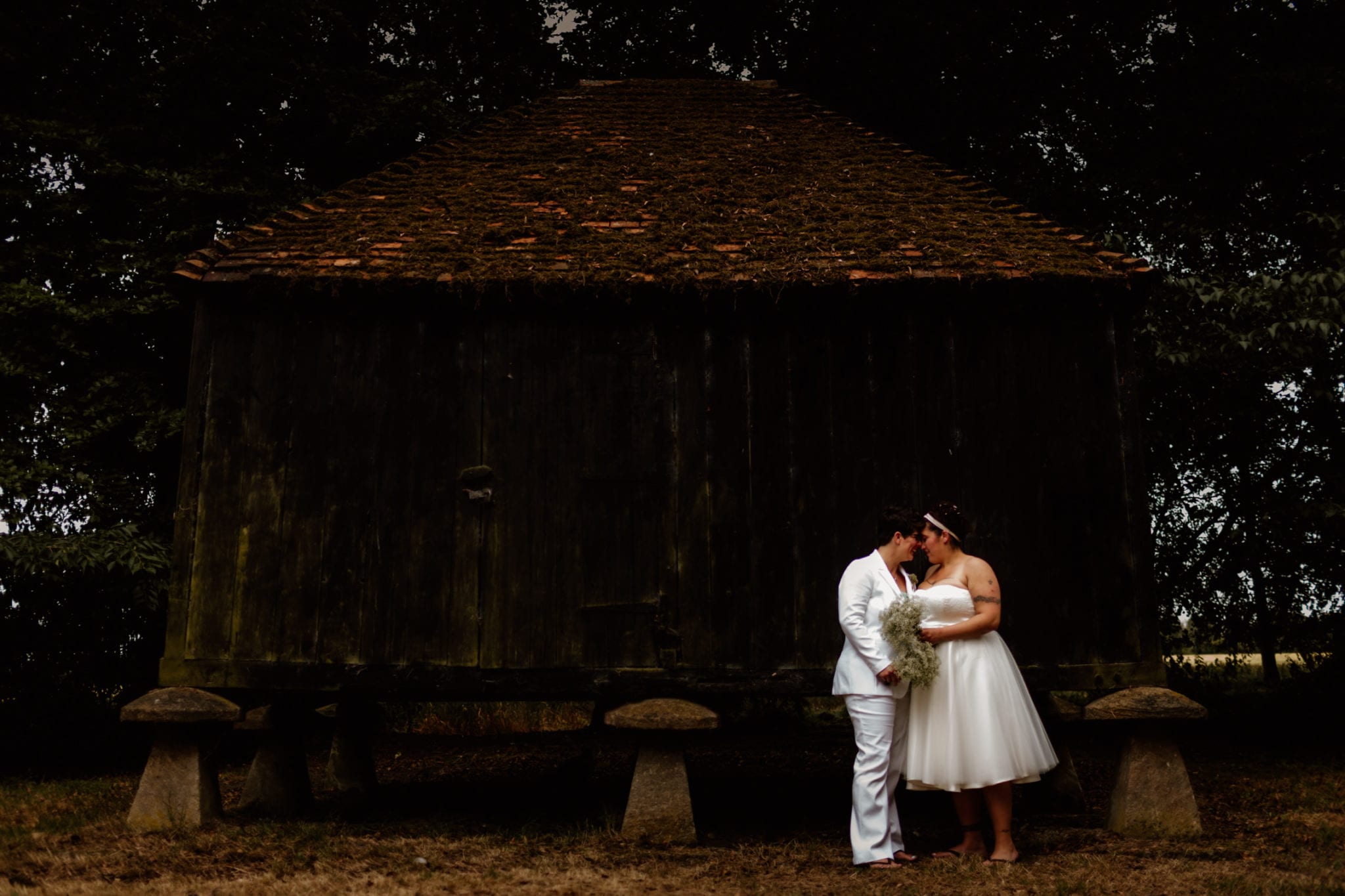 Two brides kissing outside shed at lains barn