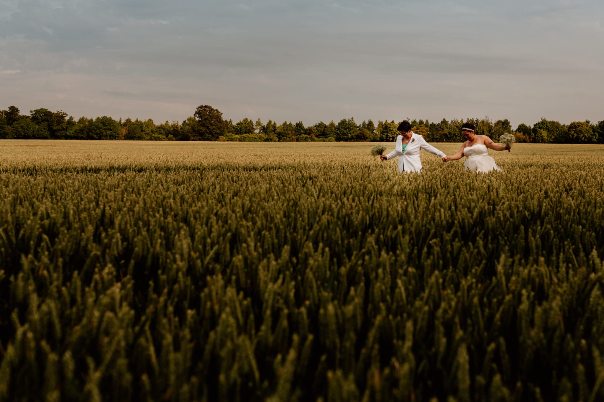 Two brides walking through corn field on their wedding day