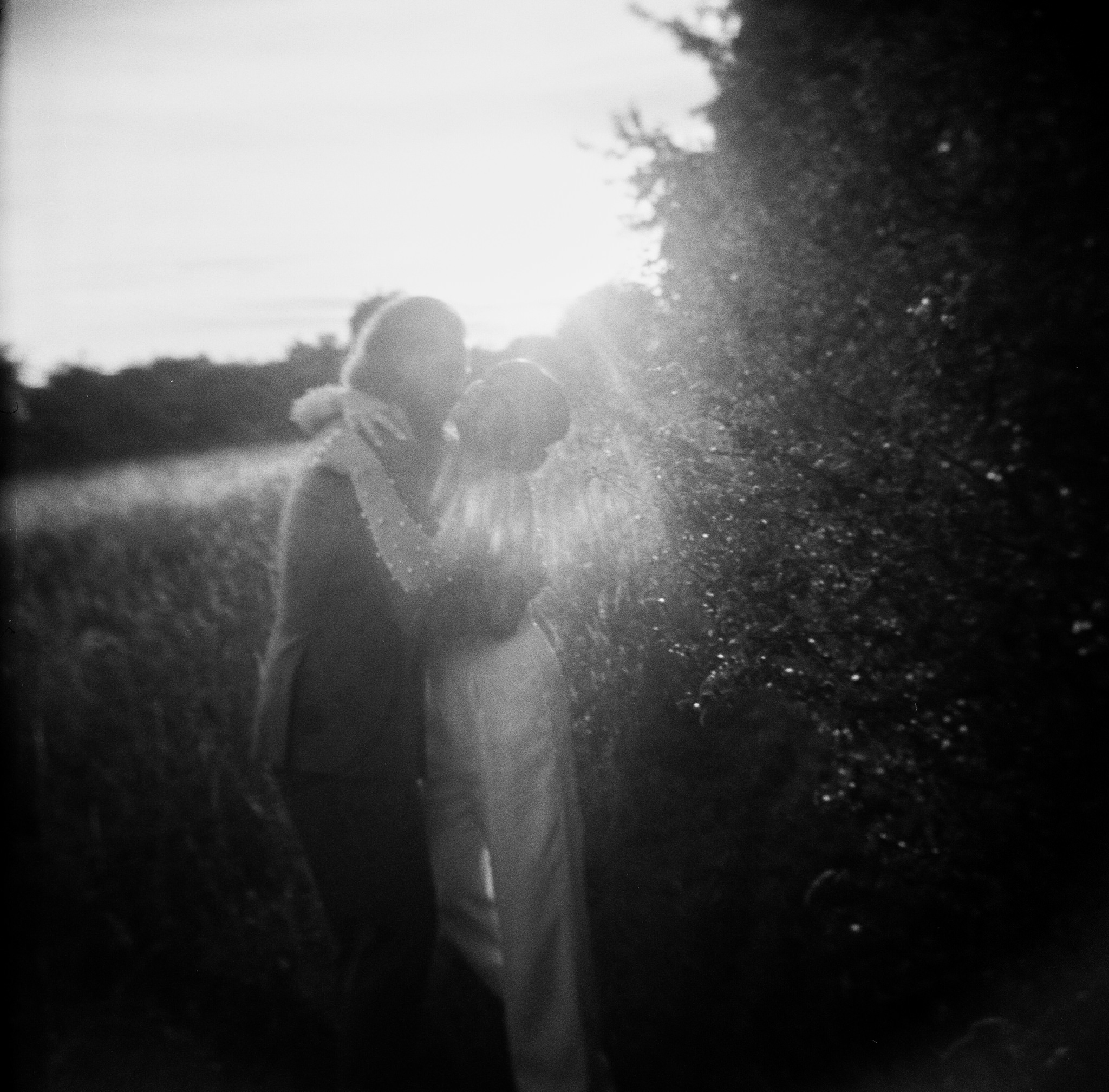 Couple pose in field, photo is black and white with heavy grain. Bedfordshire Film Photographer