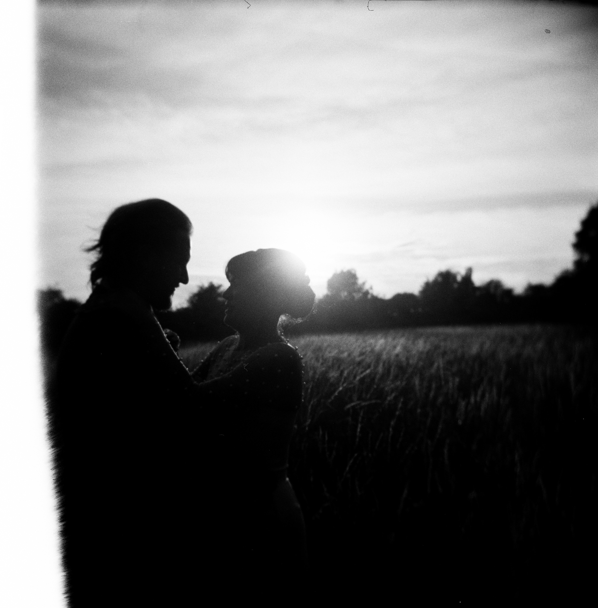Couple pose in field, photo is black and white with heavy grain. Bedfordshire Film Photographer