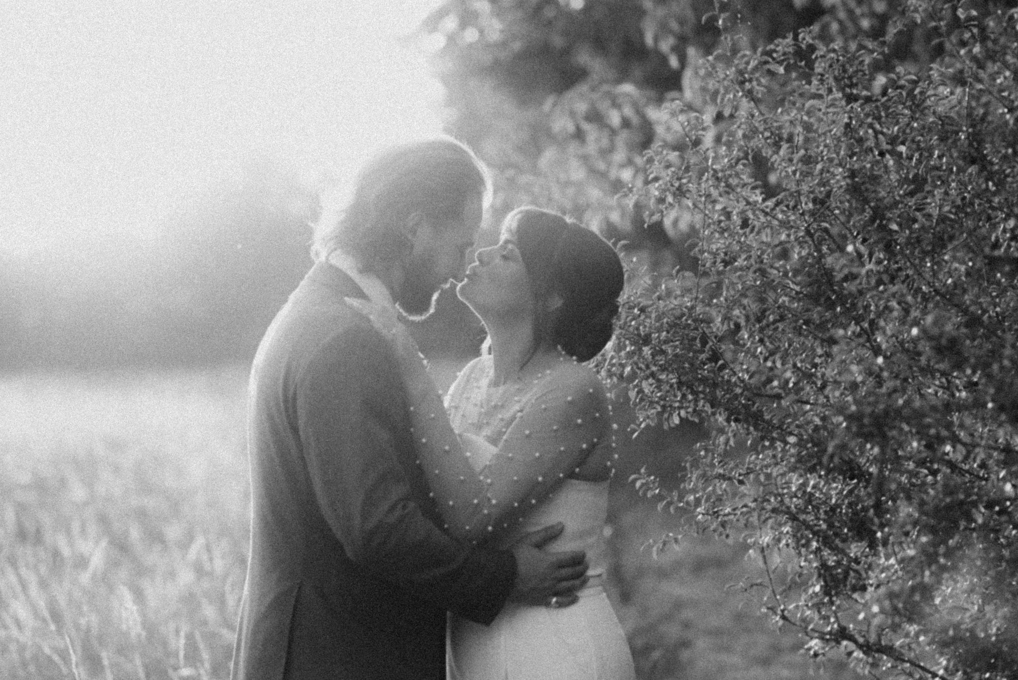 Couple pose in field, photo is black and white with heavy grain. Bedfordshire Film Photographer