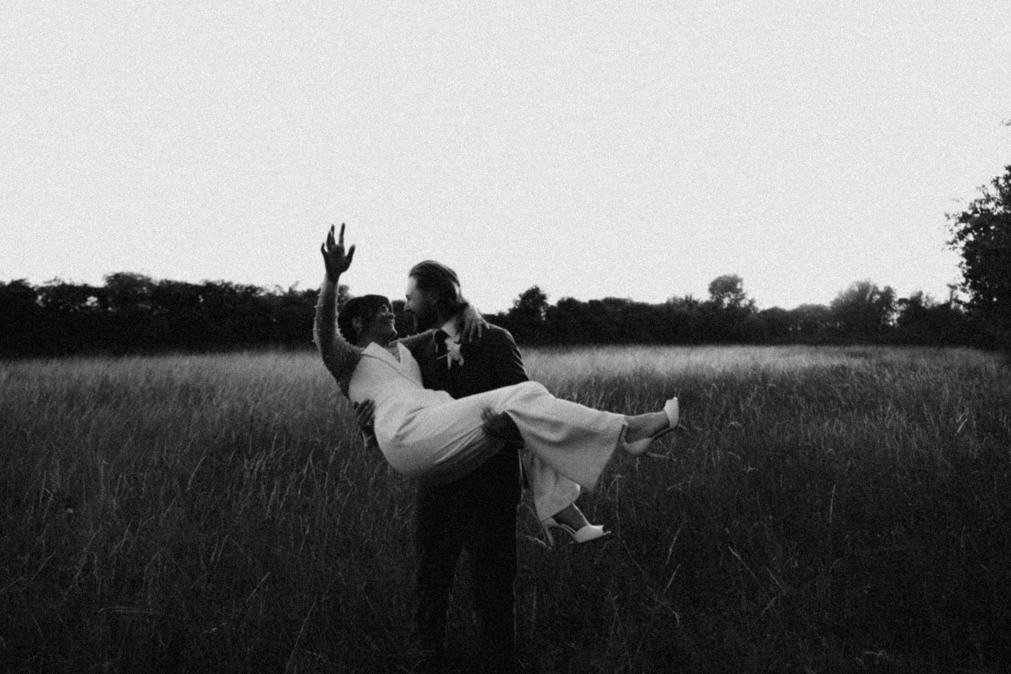 Couple pose in field, photo is black and white with heavy grain. Bedfordshire Film Photographer